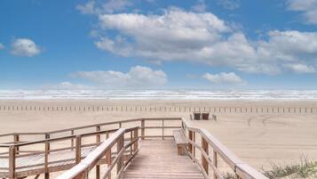 Un muelle de madera que conduce a una playa arenosa bajo un cielo despejado.