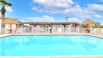 A swimming pool with a pergola and lounge chairs, surrounded by a fence and palm trees.