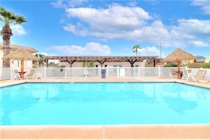 Ein Swimmingpool mit einer Pergola und Liegestühlen, umgeben von einem Zaun und Palmen.