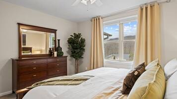 A bedroom with a bed, a dresser, a mirror, a window with curtains, and a ceiling fan.
