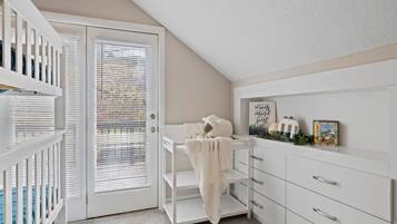 A room with a white crib, a white dresser, and a door with blinds.