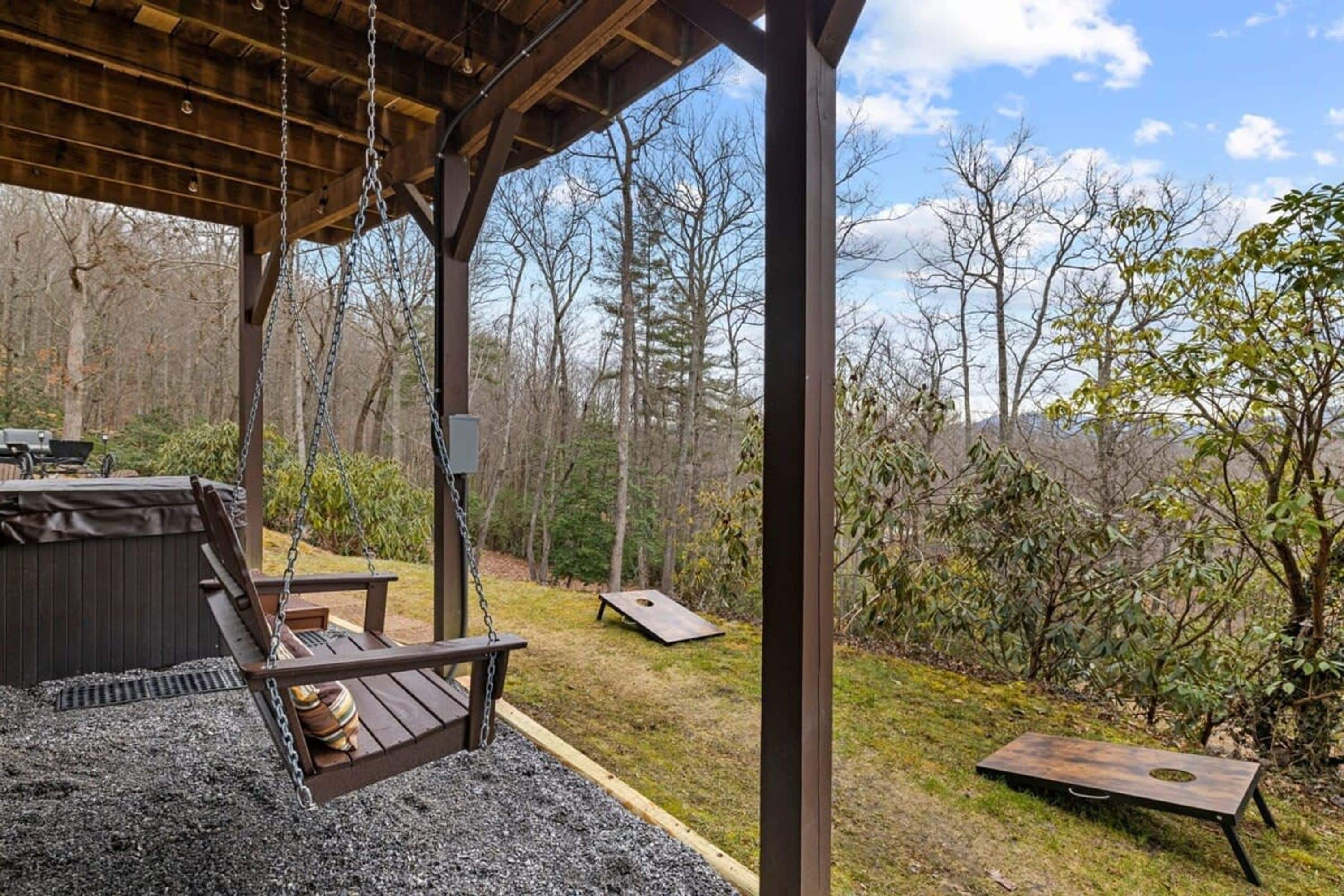 A covered outdoor area with a swing, a grill, and a view of a forest.