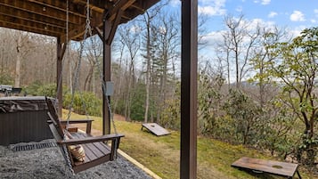 A covered outdoor area with a swing, a grill, and a view of a forest.