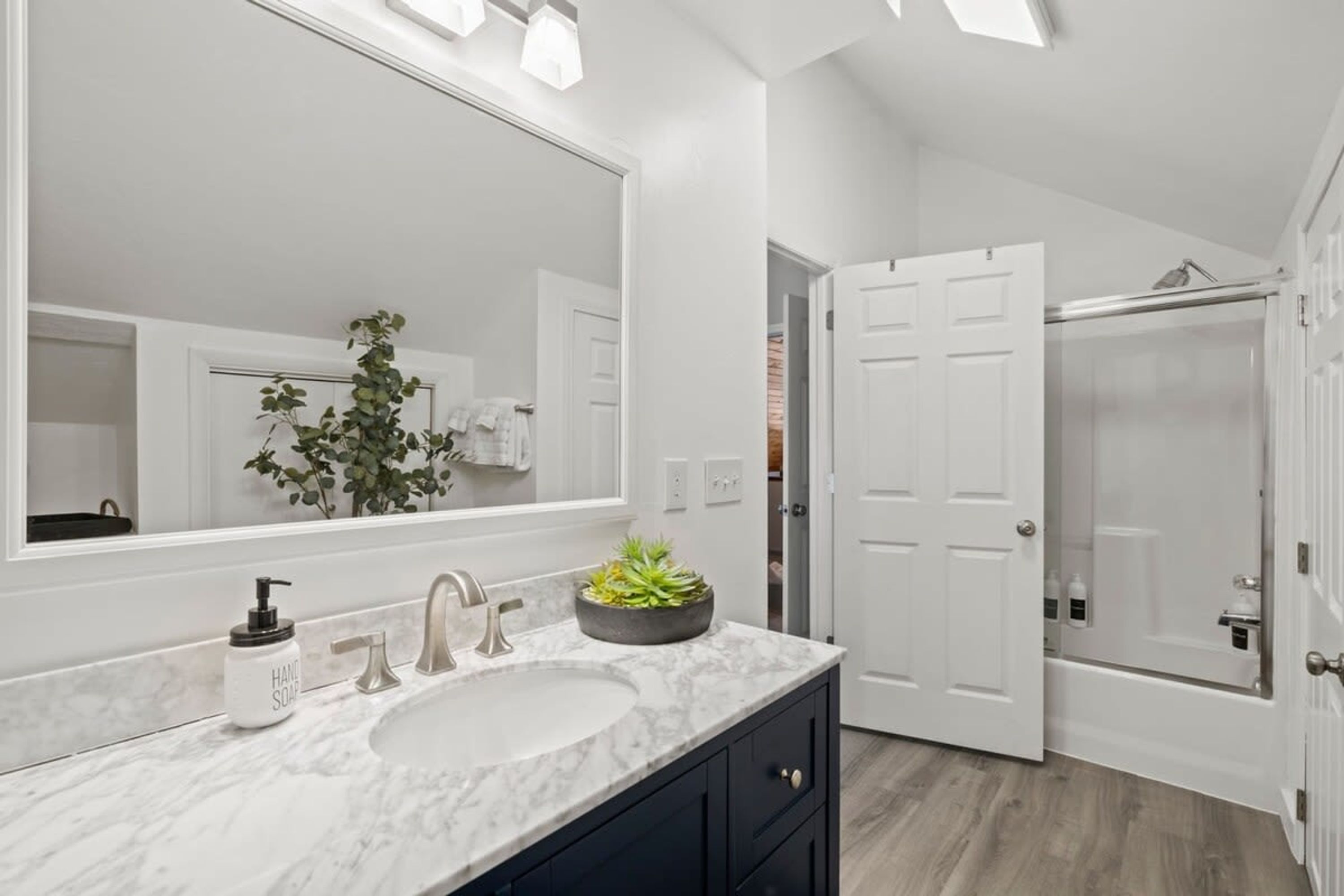 A bathroom with a large mirror, a sink, a plant, and a shower area.