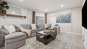 A living room with a sectional sofa, a coffee table, a rug, a painting, and a TV mounted on the wall. - 6 Br Sleeps 16 - Game Room - Hot Tub - Firepit (Fairview)