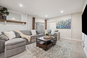 Ein Wohnzimmer mit Ecksofa, Couchtisch, Teppich, einem Gemälde und einem an der Wand befestigten Fernseher.