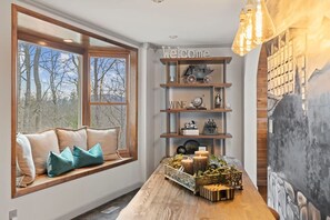 A room with a large window, a wooden table with decorative items, and a wall with a mural. - 6 Br Sleeps 16 - Game Room - Hot Tub - Firepit (Fairview)