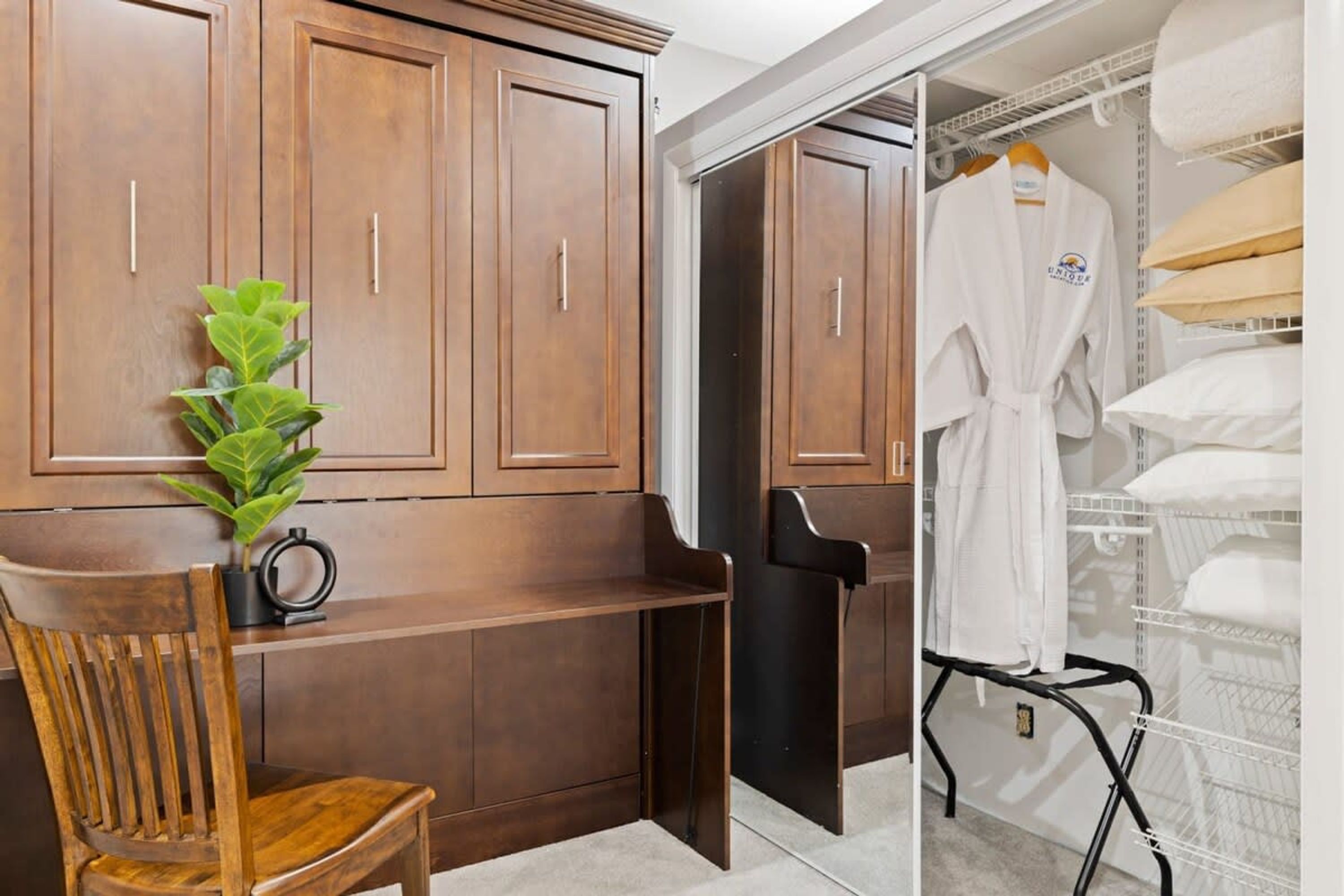 A bathroom with wooden cabinets, a chair, a potted plant, a robe hanging on a rack, and a towel rack with towels.
