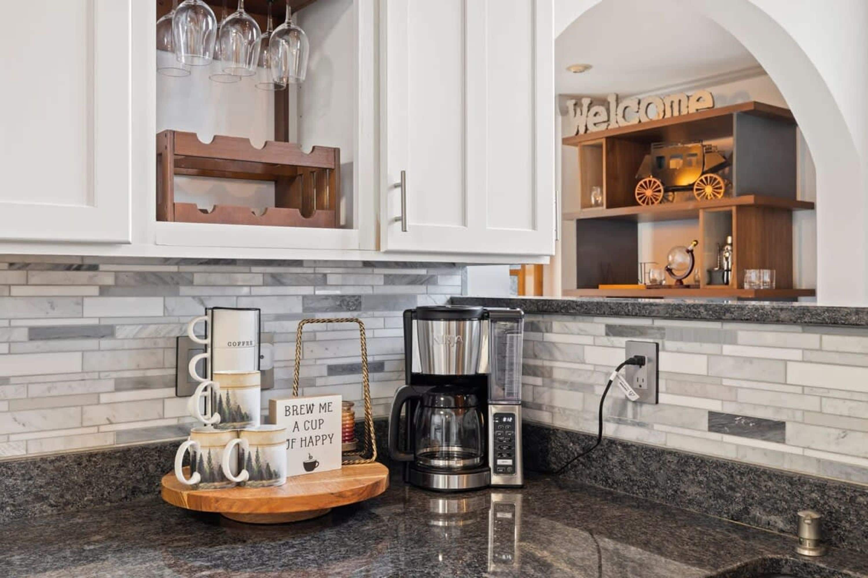 A kitchen with a coffee maker, a tray with coffee mugs, and a sign that says 'Brew me a cup if happy.'
