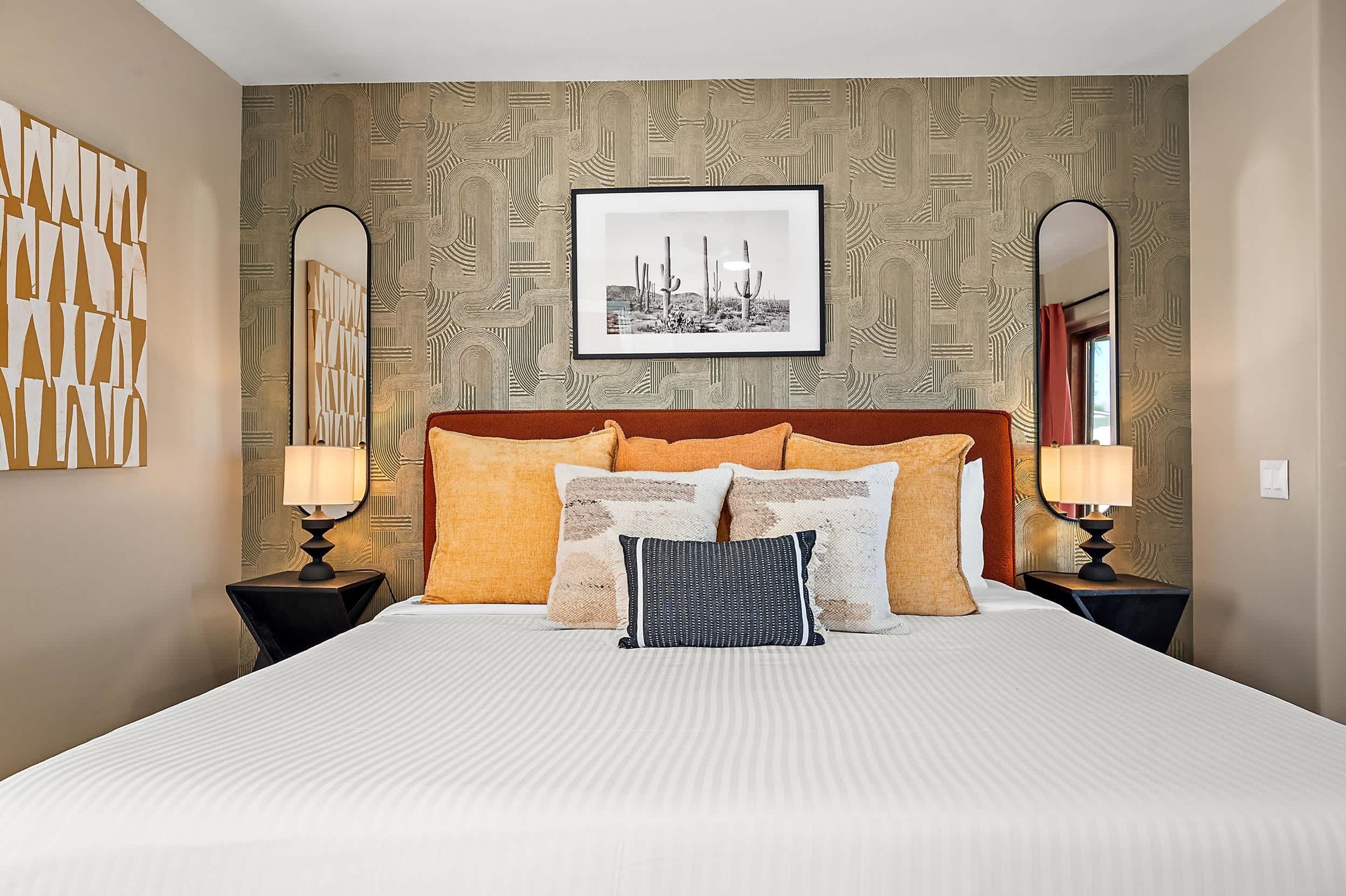 A hotel room with a large bed, two nightstands, a framed picture on the wall, and patterned wallpaper.