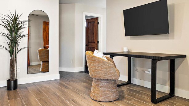 Ein modernes Interieur mit Holzboden, einem großen Spiegel, einer Sitzecke mit einem Korbstuhl und einem schwarzen Tisch.