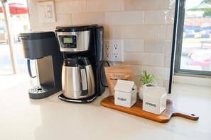 Una macchina da caffè, un contenitore per lo zucchero, un contenitore per la panna e una confezione di caffè su un bancone della cucina.