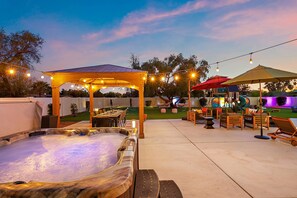 Ein Terrassenbereich im Freien mit Whirlpool, einer Holzpergola, Lichterketten und Gartenmöbeln.