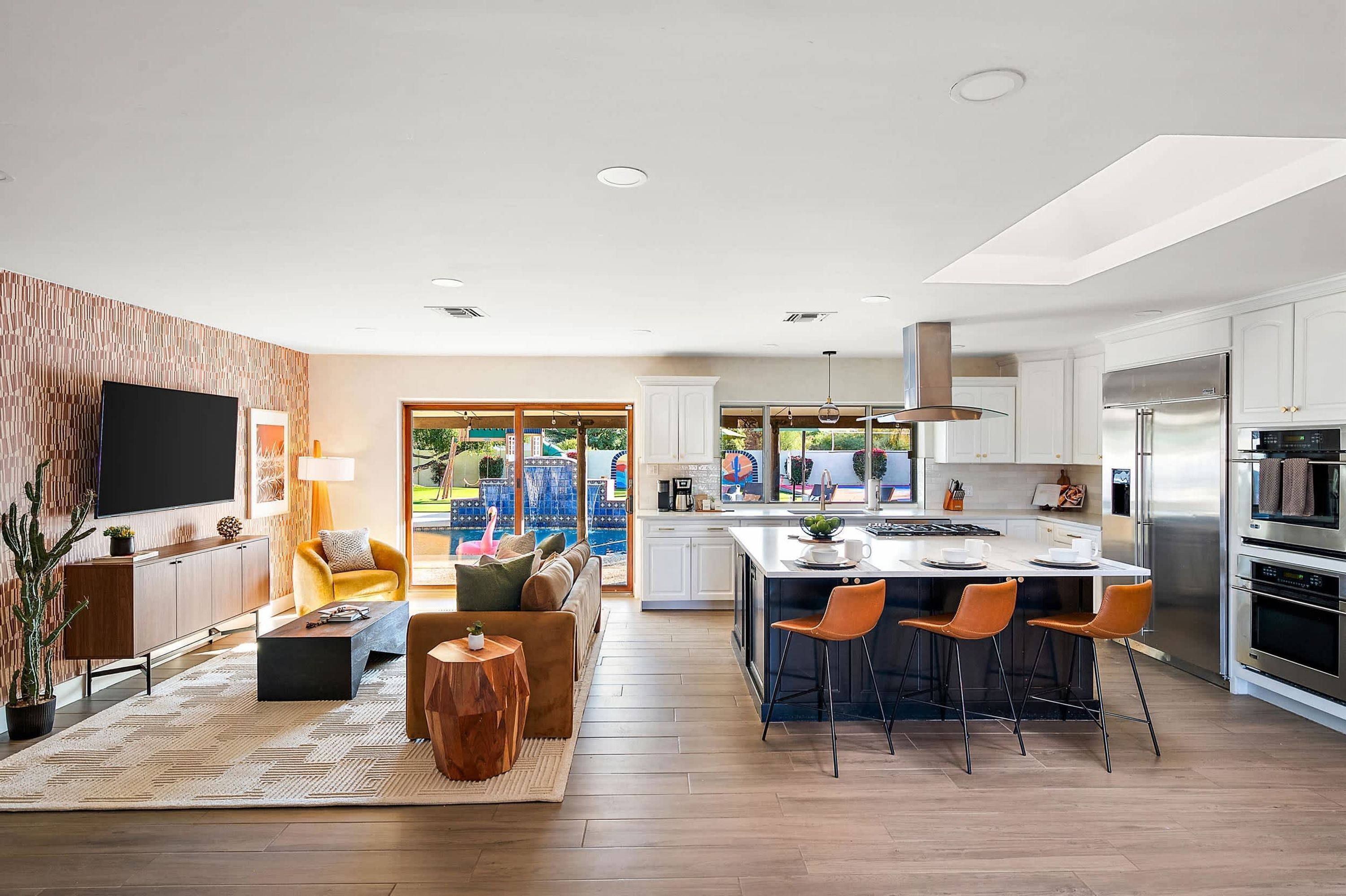 Cocina moderna con una isla central, asientos de bar y un comedor con vistas a una piscina.