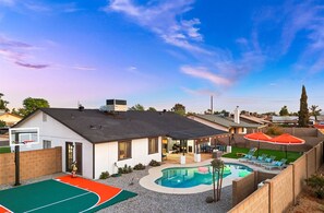 A residential backyard with a swimming pool, a basketball court, and a patio area with outdoor furniture. - The Brightside Heated Pool Bball Court Bocce (Glendale)
