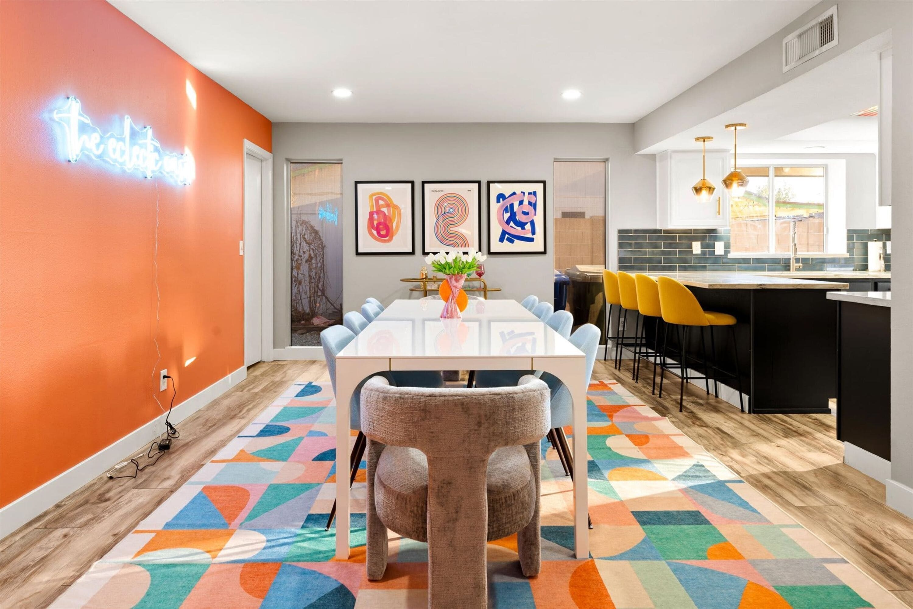 A modern kitchen with a bar area, a dining table with chairs, and colorful abstract art on the wall.