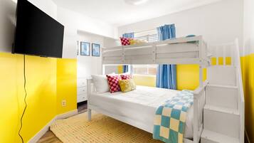 A bunk bed room with a television mounted on the wall, a window with curtains, and a yellow accent wall.
