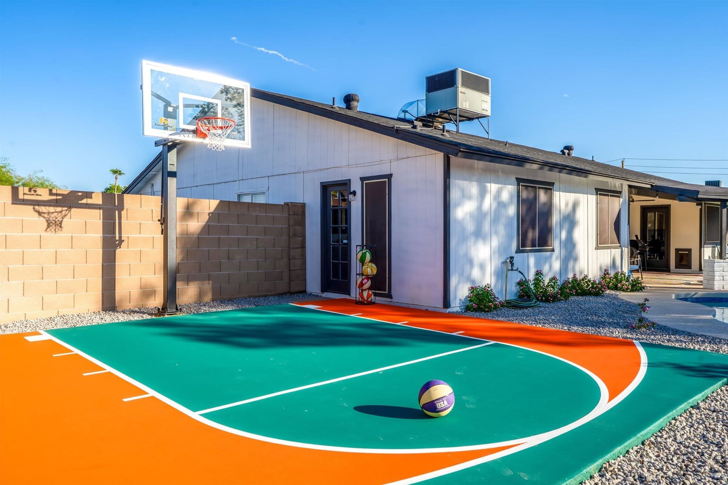 A basketball court with a hoop and a volleyball, a building with a door and windows, and a clear sky.