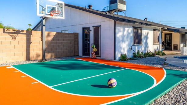 En basketballbane med ring og volleyball, en bygning med dør og vinduer, og en klar himmel.