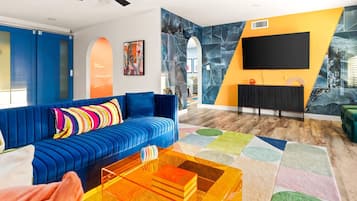 Un salon moderne avec un canapé bleu, un tapis coloré et un téléviseur à écran plat fixé sur un mur jaune.