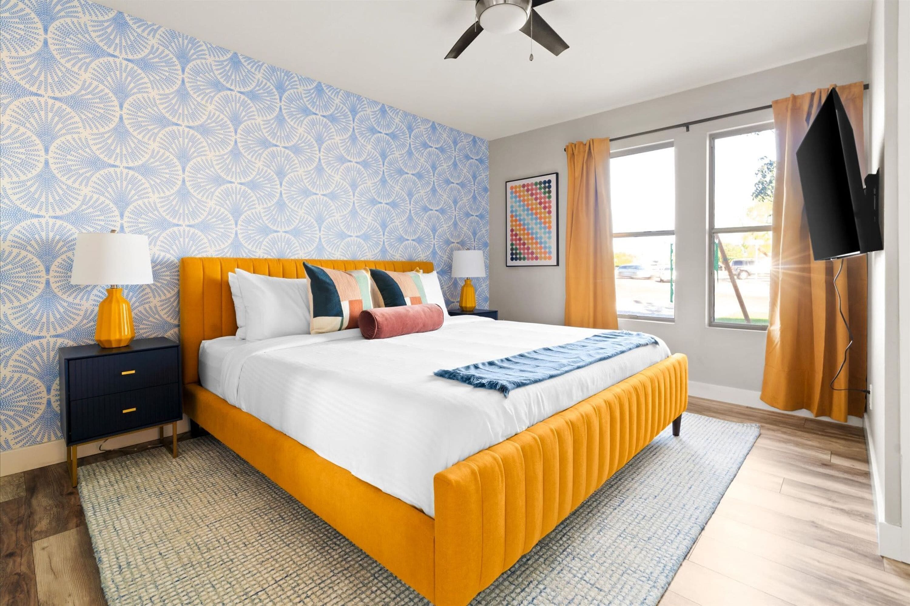 A modern bedroom with a large bed, two bedside tables, a ceiling fan, and a window with curtains.
