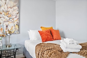 Ein Hotelzimmer mit Bett, Kissen, Decke, Lampe und einem Gemälde an der Wand.
