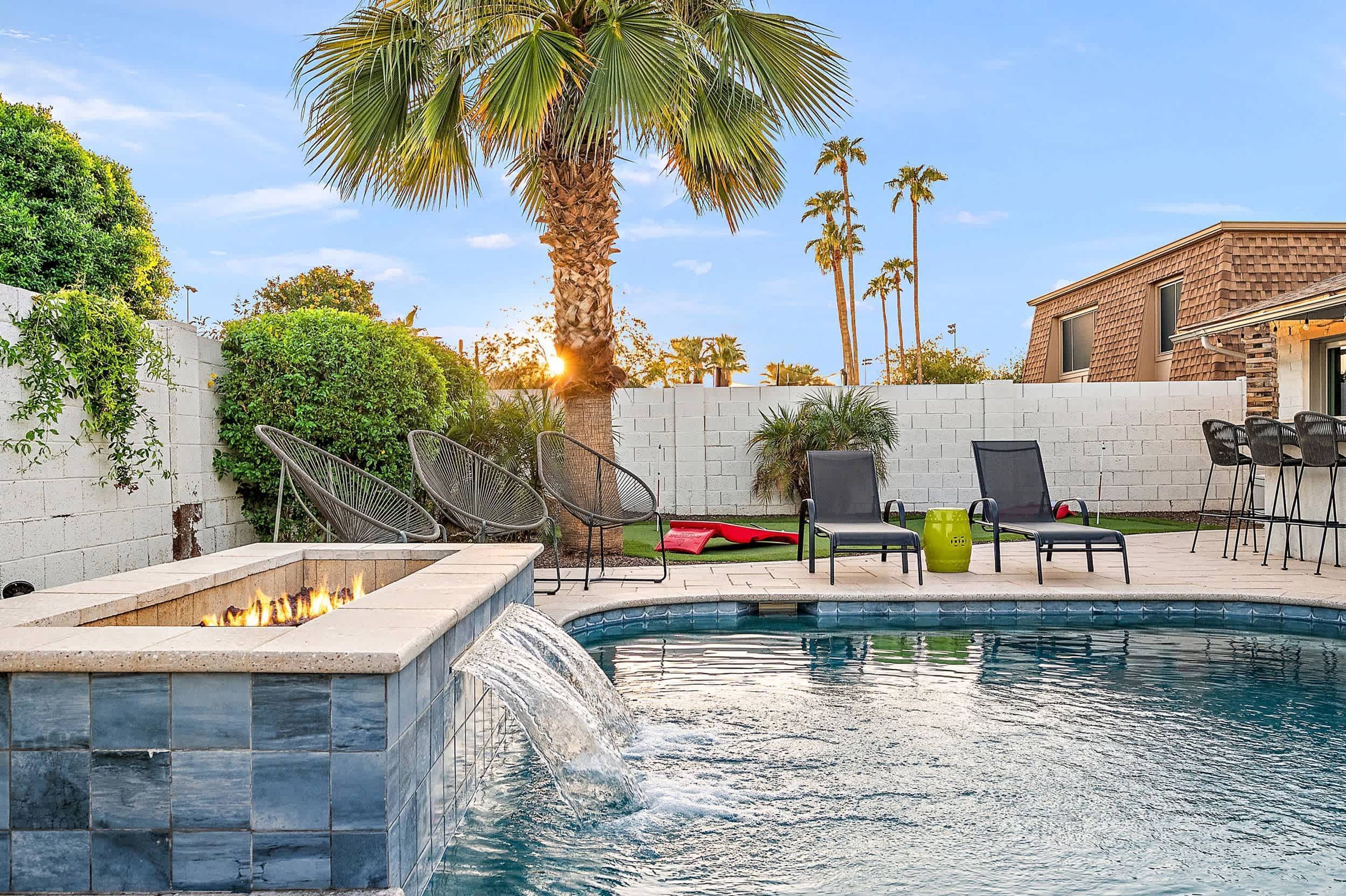 A swimming pool with a built-in fire feature, surrounded by outdoor furniture and palm trees.