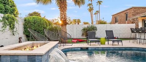 A swimming pool with a built-in fire feature, surrounded by outdoor furniture and palm trees.