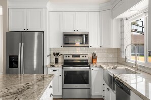 Uma cozinha moderna com eletrodomésticos de aço inoxidável, armários brancos e uma grande janela que oferece luz natural.