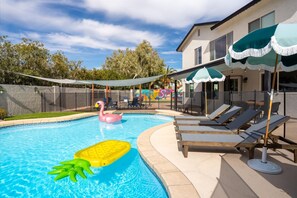 A swimming pool with lounge chairs and umbrellas, surrounded by a fence and trees. - Private Pickleball Court Movie Room Hot Tub (Scottsdale)