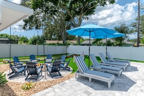 Eine Terrassenanlage im Freien mit Lounge-Möbeln, einer Feuerstelle und einem blauen Sonnenschirm.