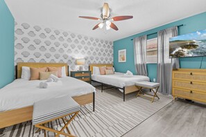 Ein Hotelzimmer mit zwei Betten, einem Deckenventilator, einem großen Fenster mit Meerblick und einer Holzkommode.