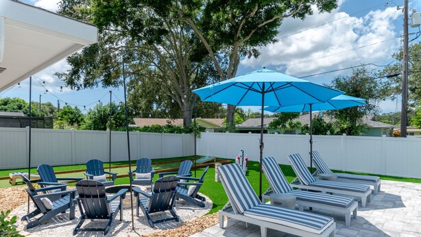 An outdoor patio with lounge chairs and a blue umbrella. - Your Beach Getaway Putt Putt Bikes Game Room BBQ (Largo)