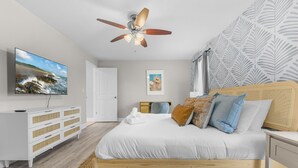 A bedroom with a bed, a ceiling fan, a TV, a dresser, and a door. - Your Beach Getaway Putt Putt Bikes Game Room BBQ (Largo)