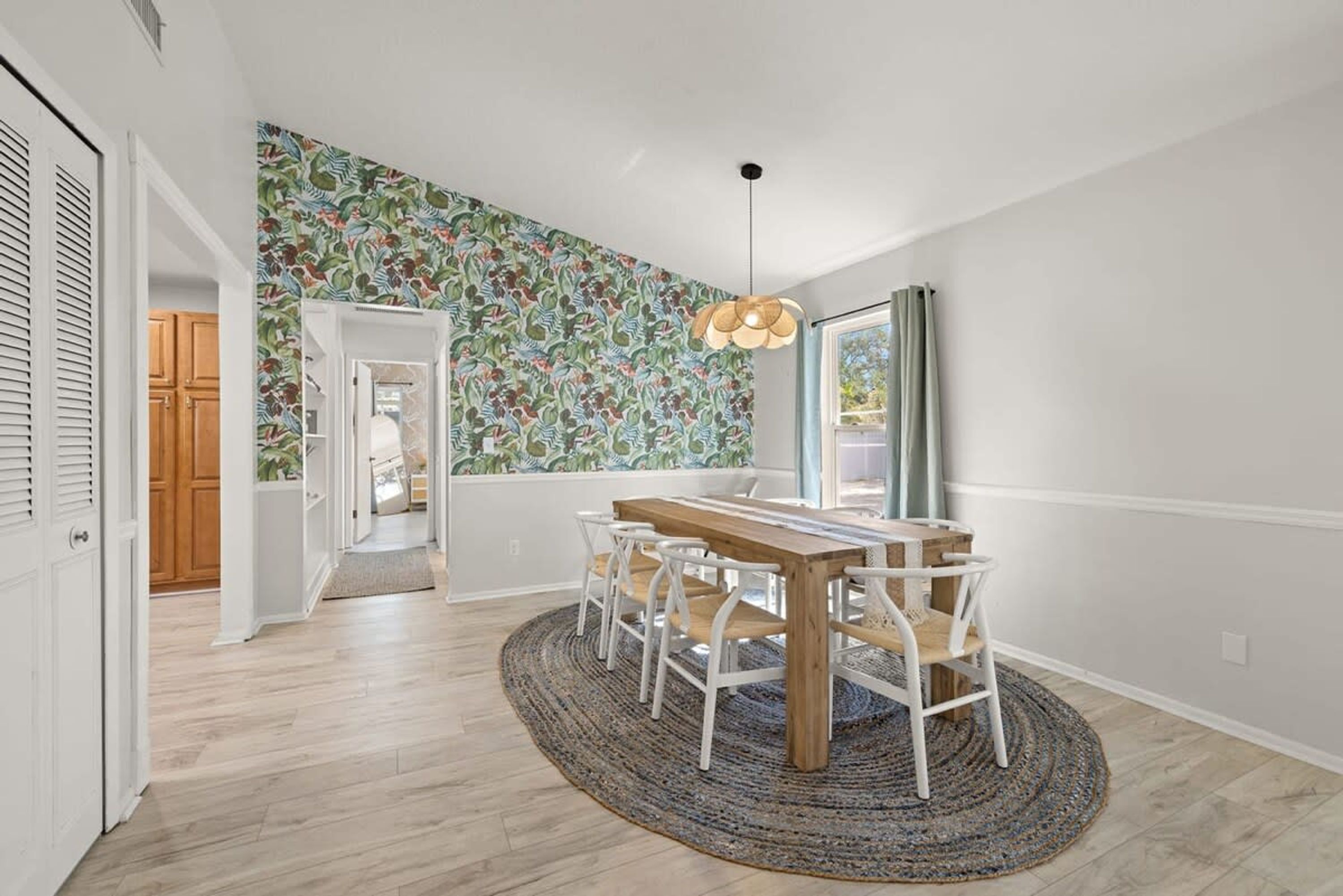 Un comedor con una mesa y sillas de madera, un papel tapiz estampado y una lámpara colgante.