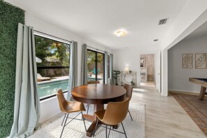 A modern dining area with a round table and chairs, a view of a swimming pool, and a hallway leading to a bathroom. - 1 Mile to Beach Private Pool Oasis Volleyball (Palm Harbor)