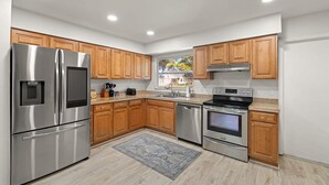 A modern kitchen with stainless steel appliances, wooden cabinets, and a large window. - 1 Mile to Beach Private Pool Oasis Volleyball (Palm Harbor)