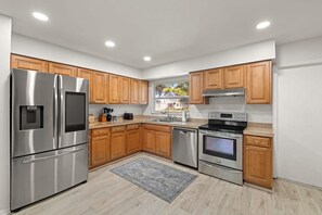 A modern kitchen with stainless steel appliances, wooden cabinets, and a large window. - 1 Mile to Beach Private Pool Oasis Volleyball (Palm Harbor)