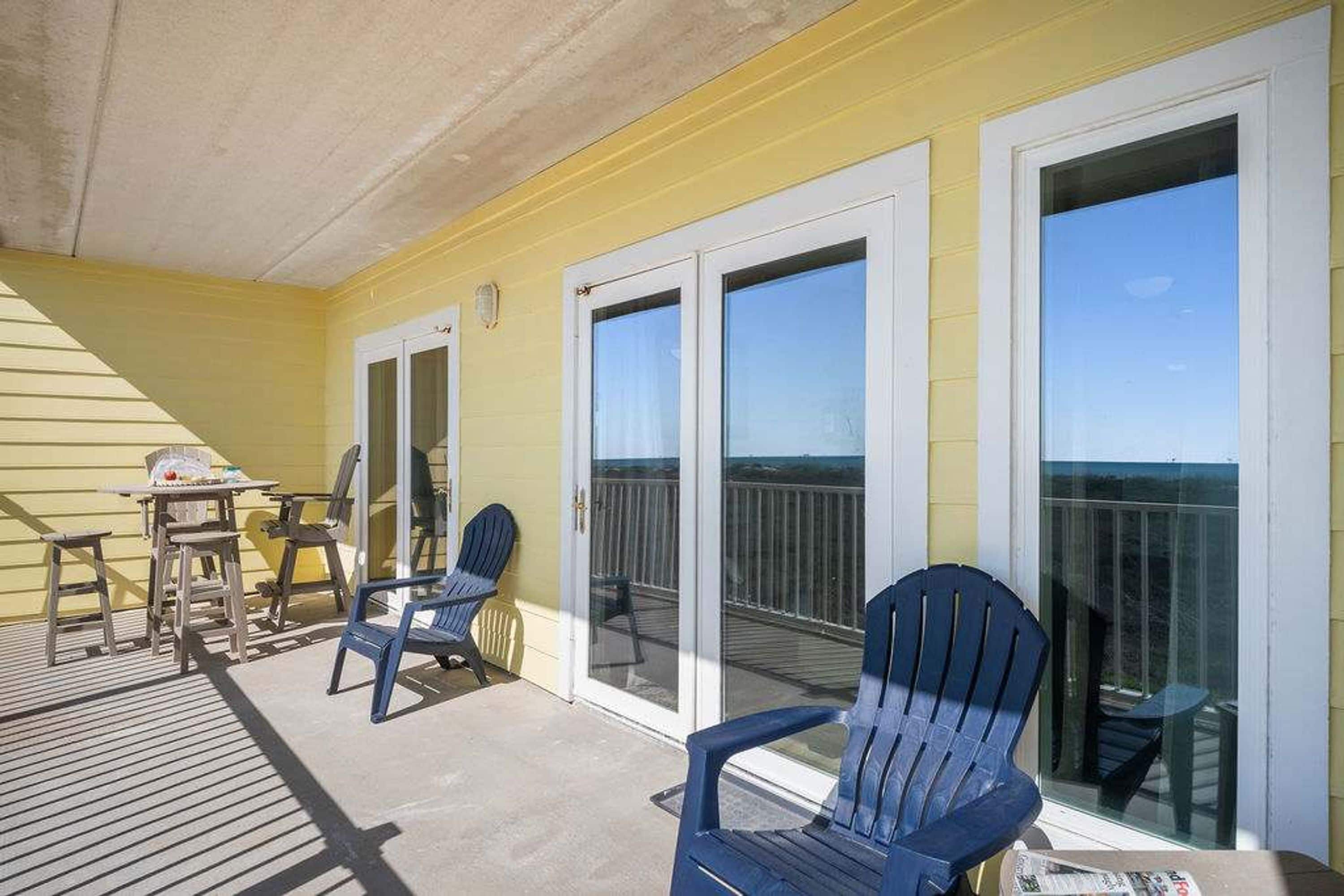 A covered outdoor area with a yellow wall, two sliding glass doors, and a wooden deck.