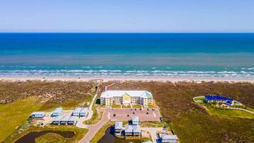 An aerial view of a coastal hotel with multiple buildings, a parking area, and a beach in the background.