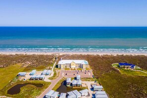 An aerial view of a coastal hotel with multiple buildings, a parking area, and a beach in the background.