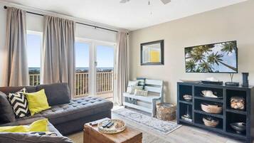 A living room with a sofa, a coffee table, a TV stand, and a view of the outdoors.