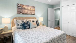 A bedroom with a bed, two bedside lamps, a ceiling fan, a door, and a wall-mounted picture. - Ocean Views Boardwalk Access Large Community Pool (Port Aransas)