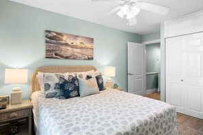 A bedroom with a bed, two bedside lamps, a ceiling fan, a door, and a wall-mounted picture. - Ocean Views Boardwalk Access Large Community Pool (Port Aransas)
