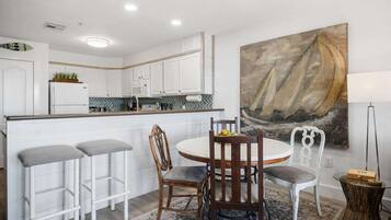 A modern kitchen with white cabinets, a central island, and a dining area with a round table and bar stools.