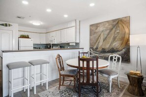 A modern kitchen with white cabinets, a central island, and a dining area with a round table and bar stools.