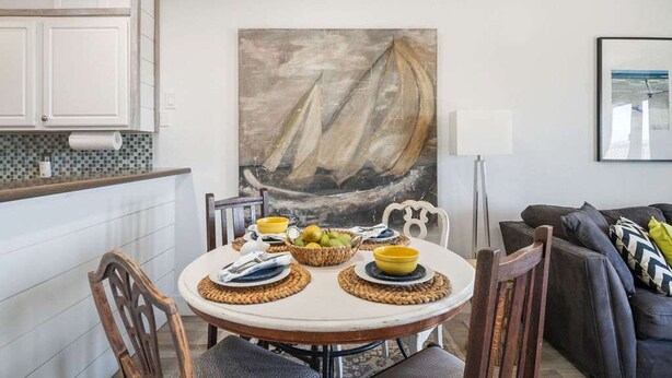 A dining area with a round table, chairs, and a painting of a sailboat. - Ocean Views Boardwalk Access Large Community Pool (Port Aransas)