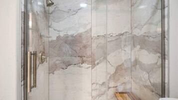A shower with marble walls and a wooden floor.