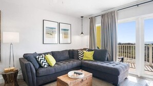 A modern living room with a sectional sofa, a round coffee table, and a view of the outdoors. - Ocean Views Boardwalk Access Large Community Pool (Port Aransas)