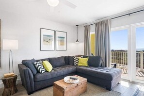 A modern living room with a sectional sofa, a round coffee table, and a view of the outdoors. - Ocean Views Boardwalk Access Large Community Pool (Port Aransas)